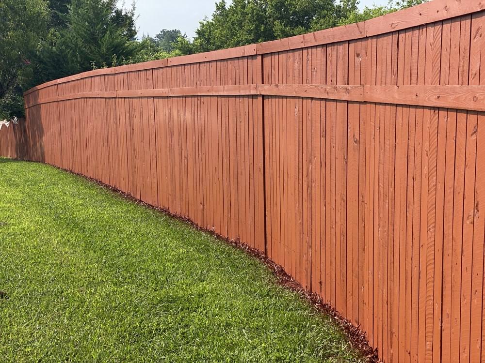 Freshly stained wood privacy fence running along a backyard